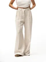 Pantalón largo de vestir color beige, tiro alto, con pliegues frontales, cierre de cremallera y botón. Presenta bolsillos laterales inclinados y bolsillos traseros ribeteados. La cintura tiene trabillas para cinturón y un elástico en la parte trasera.