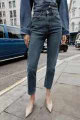 Pantalón de jean azul de tiro alto, corte mom fit, tobillero y con cinco bolsillos. Cierre frontal con cremallera y botón.