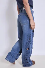 Pantalón de jean azul con bordados florales y aberturas en forma de flor en las piernas.