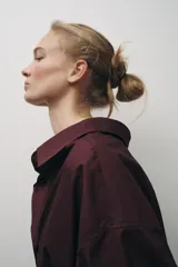 Camisa color borgoña de Zara Woman Collection, confeccionada en algodón popelín. Tiene cuello solapa, escote en pico, mangas largas con puños abotonados, bajo redondeado y cierre frontal con botones.