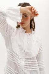 Camisa blanca de algodón con volados en el pecho y cuello, botones nacarados y mangas largas con puños elásticos.