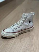 Zapatillas de lona blancas de caña alta con cordones y puntera de goma. Logo de durazno engomado en la base y en la cara interna.