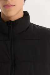 Campera acolchada negra con cuello alto y cierre frontal, de corte estándar.