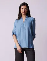 Blusa celeste en lyocell, con cuello a la base con solapa, escote en V y abertura central con botones. Manga larga regulable con presilla y botón.