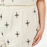 Pantalón ancho color beige con bordado de cruces negras.