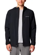 Chaqueta tipo softshell con capucha, color negro, cierre frontal completo y logo de Columbia bordado en el pecho izquierdo. Presenta puños elásticos y un dobladillo trasero más largo para mayor cobertura.