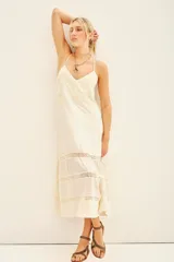 Vestido largo color blanco, de breteles finos, corte en línea A, con volado en la parte inferior y detalles de puntillas alrededor de toda la prenda.