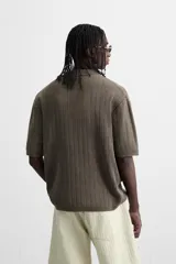 Polo marrón de punto con textura acanalada, corte relaxed fit, cuello solapa y cierre frontal con botonadura. Manga corta y terminaciones en rib. Efecto lavado.