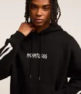 Buzo negro de fleece con felpa, corte boxy, capucha con cordón ajustable, manga larga, estampa lettering frontal, bolsillo canguro, patch de esqueleto en la manga y puños ajustados.