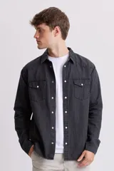 Camisa de jean de manga larga, color gris oscuro lavado, con cuello y botones a presión blancos. Presenta dos bolsillos frontales con solapa y pespuntes visibles.
