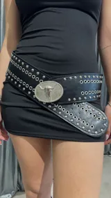 Cinturón ancho de cuero sintético negro con tachas plateadas y hebilla ovalada con diseño de cráneo de toro.