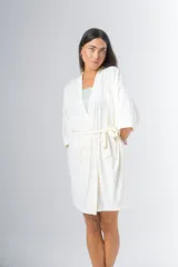 Bata tipo kimono de algodón color blanco hueso, con textura acanalada vertical. Presenta un cruce frontal asegurado con un lazo a la cintura y mangas anchas de largo al codo.