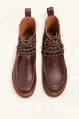 Bota de cuero vacuno color bordó con acabado brillante, diseño tipo botineta con cordones y ganchos metálicos. Presenta suela de goma tipo crepe con plataforma y costuras visibles en la puntera.