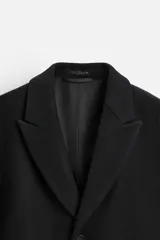Abrigo negro regular fit confeccionado en paño con lana. Tiene cuello con solapas de muesca, manga larga, bolsillos de solapa en la cadera, bolsillo interior, abertura en el centro de la espalda y cierre frontal con botonadura.