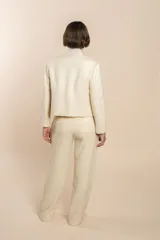 Chaqueta de sastrería color crudo con textura tweed, corte entallado, cuello mao y mangas largas.