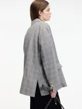 Blazer gris a cuadros con solapas de muesca, cierre con dos botones y corte holgado. Incluye un prendedor de flor negra en la solapa.