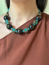 Collar corto con cuentas grandes de madera color marrón oscuro, separadores de metal con incrustaciones de turquesas y cuentas pequeñas turquesas. Cierre con cadena de acero quirúrgico y ganchito para regular el largo.