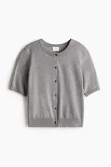 Cárdigan gris de punto fino con cuello redondo, manga corta y cierre frontal con botones. Tiene terminaciones acanaladas en cuello, puños y ruedo.