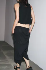 Falda midi negra de tiro alto con cintura elástica y frunces. Presenta detalle de tejido combinado y abertura en la parte trasera del ruedo.