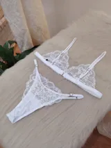 Conjunto de lencería blanco de encaje, compuesto por un bralette triangular con breteles regulables y una tanga regulable de corte less con entrepierna de algodón.