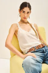 Top bretelero blanco con escote en V, ribetes de puntilla a tono en escote, breteles y sisas. Presenta tachas termoadhesivas distribuidas en el frente.