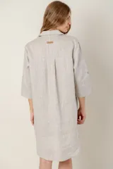 Vestido camisero negro de lino con botones, mangas 3/4 con trabilla y bolsillo de parche en el pecho con bordado de letras. Tiene aberturas laterales en el ruedo y costuras a contratono en color crudo.