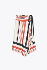 Falda midi de tiro medio con estampado de rayas rojas, negras y blancas. Tiene bajo asimétrico y cierre frontal tipo pareo ajustable con lazos negros.