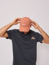 Gorra de lona color salmón con logo de la marca bordado en blanco.