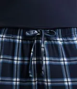 Conjunto de pijama largo para hombre, compuesto por una remera de manga corta azul marino con bolsillo en el pecho y un pantalón largo con cintura elástica y estampado de cuadros azules y blancos.