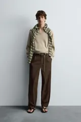 Pantalón relaxed fit color marrón confeccionado en tejido de algodón con estructura twill. Cintura con pliegues frontales, bolsillos laterales en cadera y detalle de bolsillos traseros de doble vivo con botón. Cierre frontal con cremallera y botón.