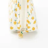 Neceser de tela color beige con estampado de limones amarillos y hojas verdes. Tiene forma ovalada y cierre superior con cremallera.