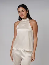 Blusa color crema de poliéster con textura plisada, cuello alto y corte sin mangas. Presenta cierre de botón y ojo de cerradura en la parte posterior del cuello y bajo con acabado ondulado.