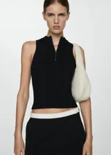 Top negro de punto acanalado, sin mangas, con cuello polo y cremallera metálica frontal.
