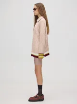 Sweater tejido de algodón color rosa claro, con cuello polo con cierre de cremallera metálica y mangas largas con puños a rayas de colores.