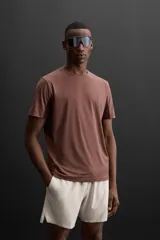 Camiseta deportiva marrón de corte relaxed fit, cuello redondo y manga corta. Presenta paneles laterales de malla negra y logo estampado en la espalda.