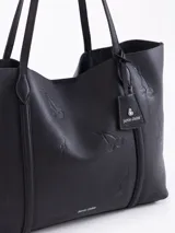 Cartera shopper negra de cuero vacuno flor, con grabados de cerezas distribuidos en la superficie. Tiene acceso mediante imán, manijas de cuero y un tag con mini aplique de cereza. Incluye un bolsillo desmontable con cierre metálico en su interior.