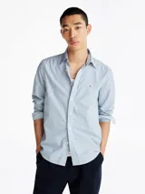 Camisa de manga larga Tommy Hilfiger, corte regular, confeccionada en popelín de algodón a rayas verticales celestes y blancas. Tiene cuello abotonado, puños redondeados con botón y logo de la marca bordado en el pecho.