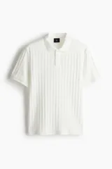 Remera polo blanca de punto texturizado de peso medio. Modelo de manga corta con cuello, tapeta de botones y bajo recto. Corte ajustado que realza el contorno del cuerpo creando una silueta entallada.