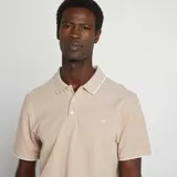 Remera polo color beige de piqué de algodón, con cuello clásico con borde blanco, tapeta de dos botones y mangas cortas con borde blanco.