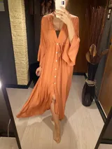 Vestido largo color naranja, con escote en V, mangas largas acampanadas, cierre frontal con botones y lazo ajustable en la cintura.