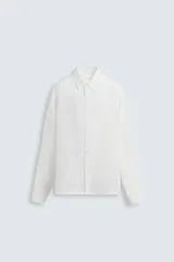 Camisa blanca de manga larga con cuello solapa y botonadura frontal. Presenta una textura ligera y un calce regular.