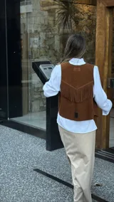 Chaleco marrón de cuero descarne con terminación en picos, tachas metálicas y flecos en la espalda.