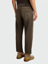 Jeans de hombre de corte recto, tiro medio, color marrón oscuro o negro lavado con efecto piedra. Presentan costuras en hilo amarillo y acabado ligeramente recortado en el tobillo.