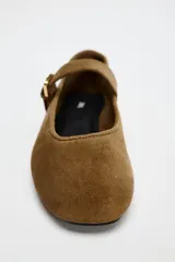 Zapato plano tipo bailarina color marrón de serraje, con escote redondo y cierre mediante hebilla en el empeine.