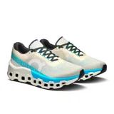 Championes de running On Running Cloudmonster 2, color crema con detalles en turquesa y verde. Presentan el logo de la marca en el lateral y suela con tecnología CloudTec.