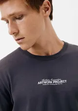 Camiseta blanca de algodón con cuello redondo y mangas cortas. Estampa rectangular con borde negro que contiene la frase "NATURAL ATMOSPHERE" en letras mayúsculas y una imagen de montañas y mar.