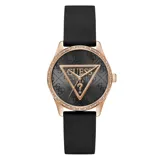 Reloj Guess con caja de metal color oro rosado, bisel decorado con cristales y correa de silicona negra. La esfera es negra con patrón de monograma y un triángulo central con el logo de Guess.