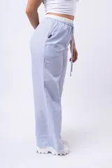Pantalón de tela a rayas verticales celestes y blancas, con corte amplio, cintura elástica y cordón ajustable.