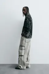 Pantalón relaxed fit de denim negro con efecto lavado, bolsillos frontales, traseros de plastrón y multifunción en perneras. Bajo ajustable con trabilla y cierre frontal con cremallera y botón.