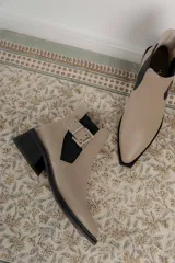 Botines Chelsea color beige con elásticos laterales negros, punta cuadrada, detalle de hebilla lateral y tacón bloque bajo.